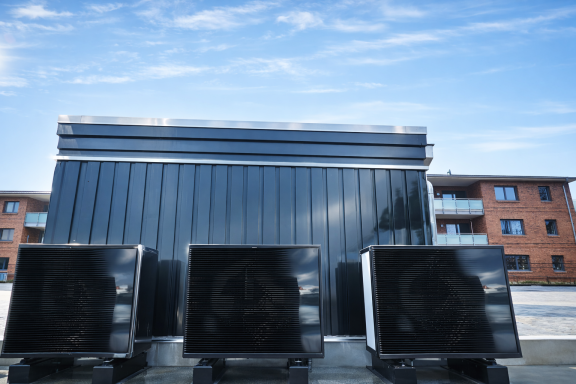 Drei schwarze Geräte vor einem modernen Gebäude unter blauem Himmel.